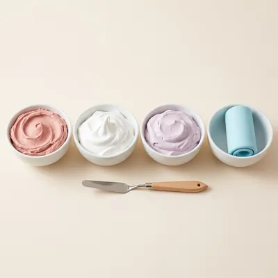 Cuatro tazones con distintas cremas de colores y fondant celeste, con una espátula